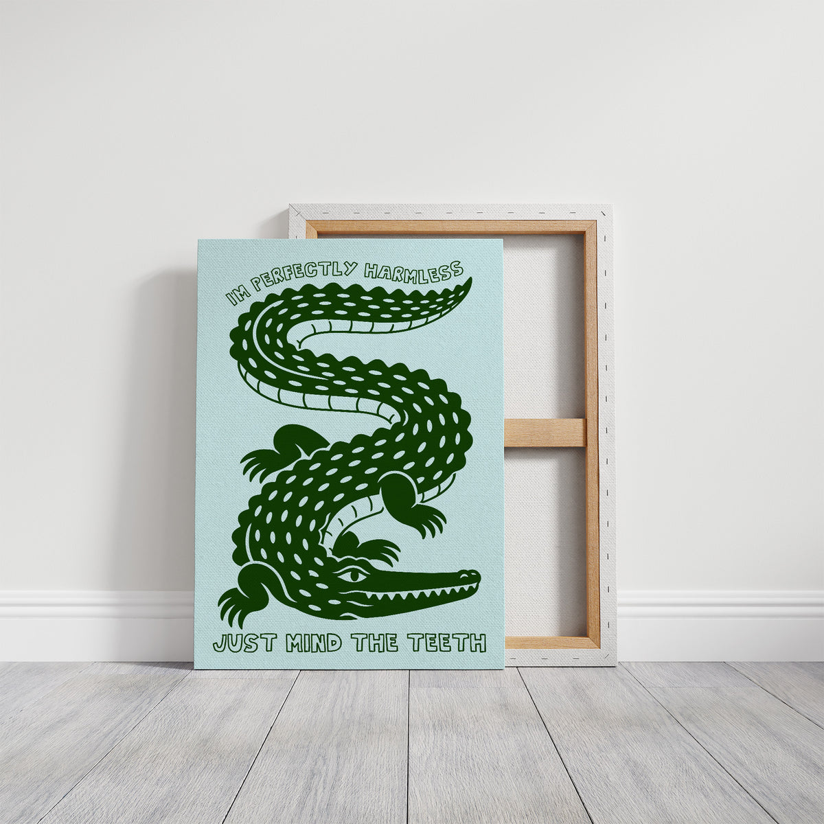 Perfectly Harmless, Mind the Teeth, a deep green crocodile curling down a pale mint ground, with a bold hand lettered line above reading I'M PERFECTLY HARMLESS and one below reading JUST MIND THE TEETH, on a gallery canvas with wrapped edges leaning against a white wall