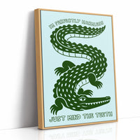 Perfectly Harmless, Mind the Teeth, a deep green crocodile curling down a pale mint ground, with a bold hand lettered line above reading I'M PERFECTLY HARMLESS and one below reading JUST MIND THE TEETH, as a framed canvas in a natural wood frame