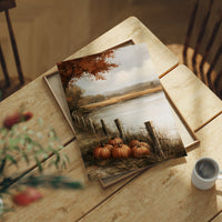 Quiet Water at the Fence Line, weathered fence posts and orange pumpkins on a grassy bank beside a misty lake, with a russet tree leaning over the water, painted in soft ochre, rust and pale gray, lying flat on a light wood table beside a coffee cup and red berries