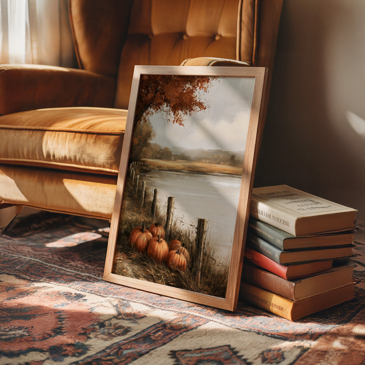 Quiet Water at the Fence Line, weathered fence posts and orange pumpkins on a grassy bank beside a misty lake, with a russet tree leaning over the water, painted in soft ochre, rust and pale gray, in a wood frame on a rug beside a leather armchair and a stack of books