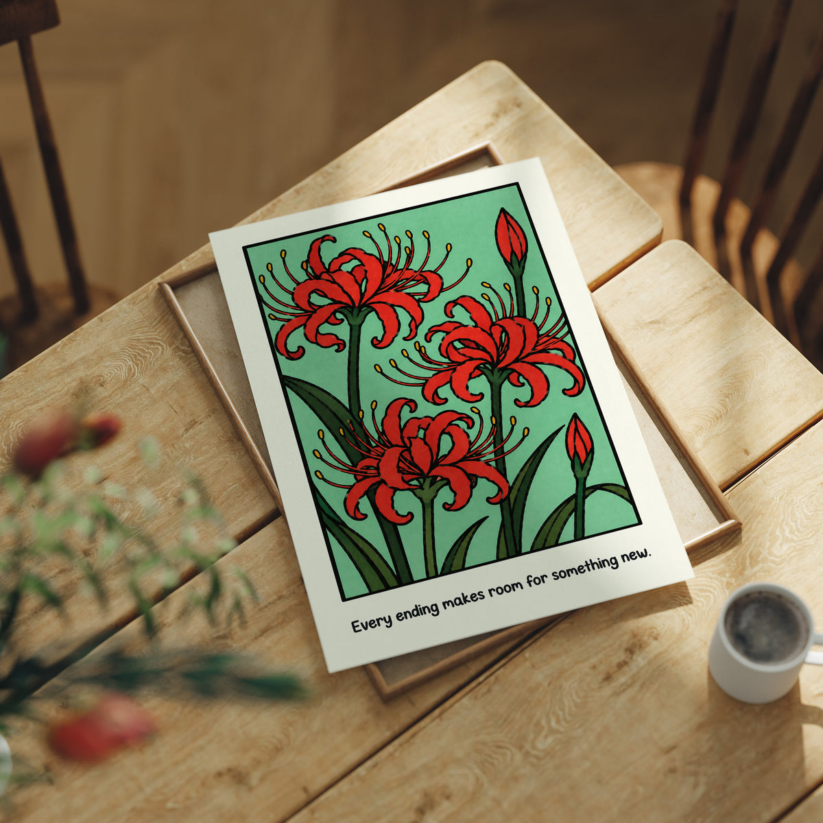 Red Lilies Make Room for Something New, red spider lily blooms with buds and dark green stems on a soft green ground, with the words Every ending makes room for something new in small black lettering along the bottom, lying flat on a light wood table beside a coffee cup and red berries