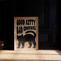 Sleek Silhouette, Questionable Taste, a solid black cat silhouette with a long tail curled up the side, standing on tan paper with the words GOOD KITTY BAD CHOICES in bold black lettering, in a dark frame on a black paneled wall above a sunlit herringbone floor