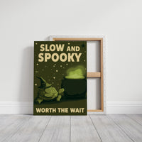 Slow and Spooky, Worth the Wait, a green cartoon creature in a witch hat beside a bubbling cauldron, bold cream lettering reading SLOW AND SPOOKY WORTH THE WAIT, on a gallery canvas with wrapped edges leaning against a white wall