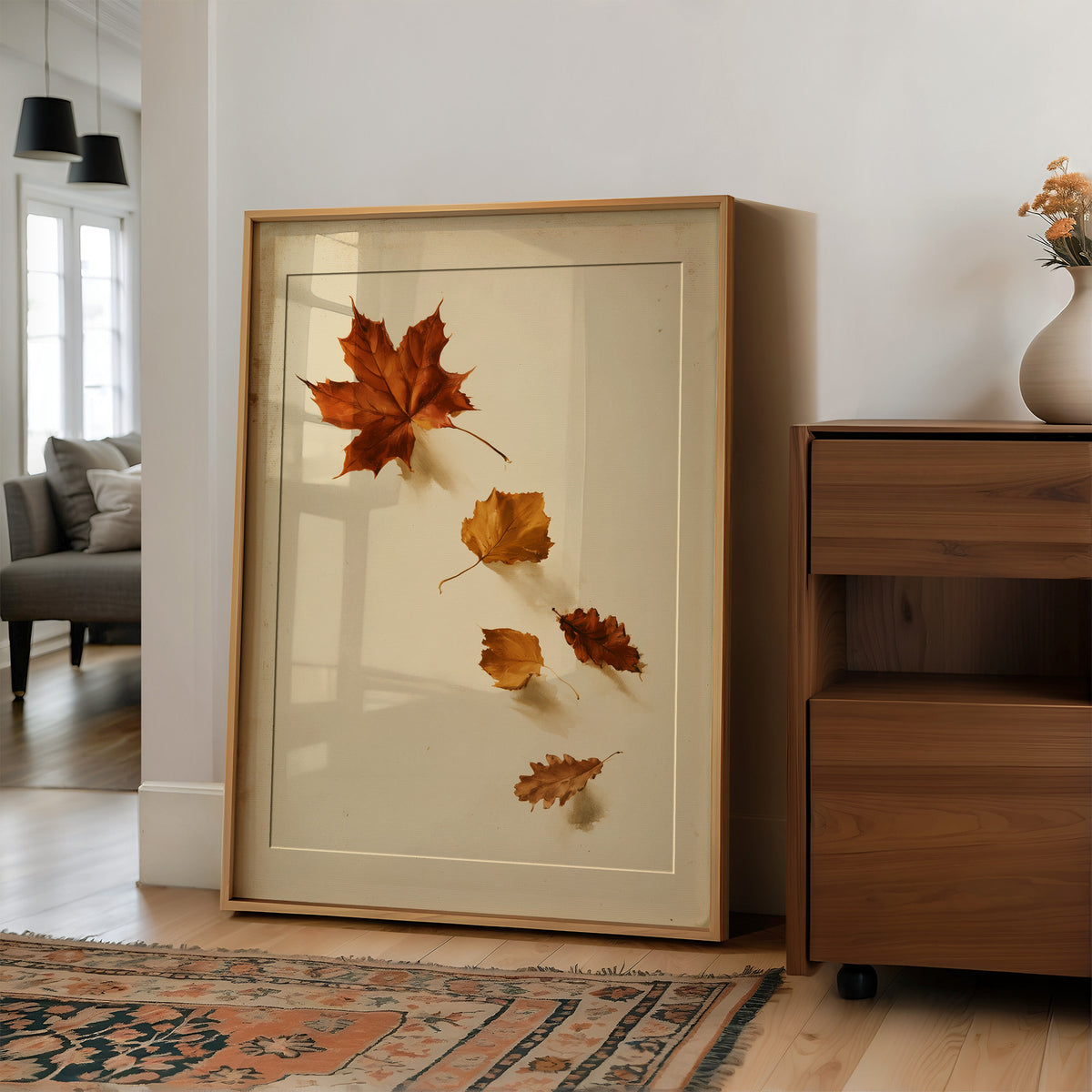 Slow Descent of the Maples, a trail of maple leaves in rust, amber and gold drifting diagonally across a warm beige ground, in a wood frame on a wall beside a walnut cabinet and an open doorway