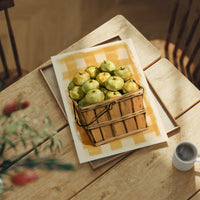 Something Sweet Waits in the Basket, a basket heaped with pale green pears on a soft yellow gingham ground, painted in lemon, sage and warm tan, lying flat on a light wood table beside a coffee cup and red berries