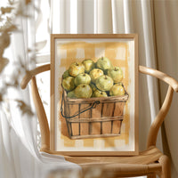 Something Sweet Waits in the Basket, a basket heaped with pale green pears on a soft yellow gingham ground, painted in lemon, sage and warm tan, in a wood frame beside a wicker chair by a sunny window