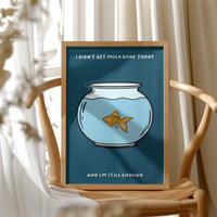 Still Enough for Today, a round glass fishbowl with one goldfish on a deep navy ground, a line of cream lettering above and below in a cartoon style, painted in navy, pale blue and orange, in a wood frame beside a wicker chair by a sunny window
