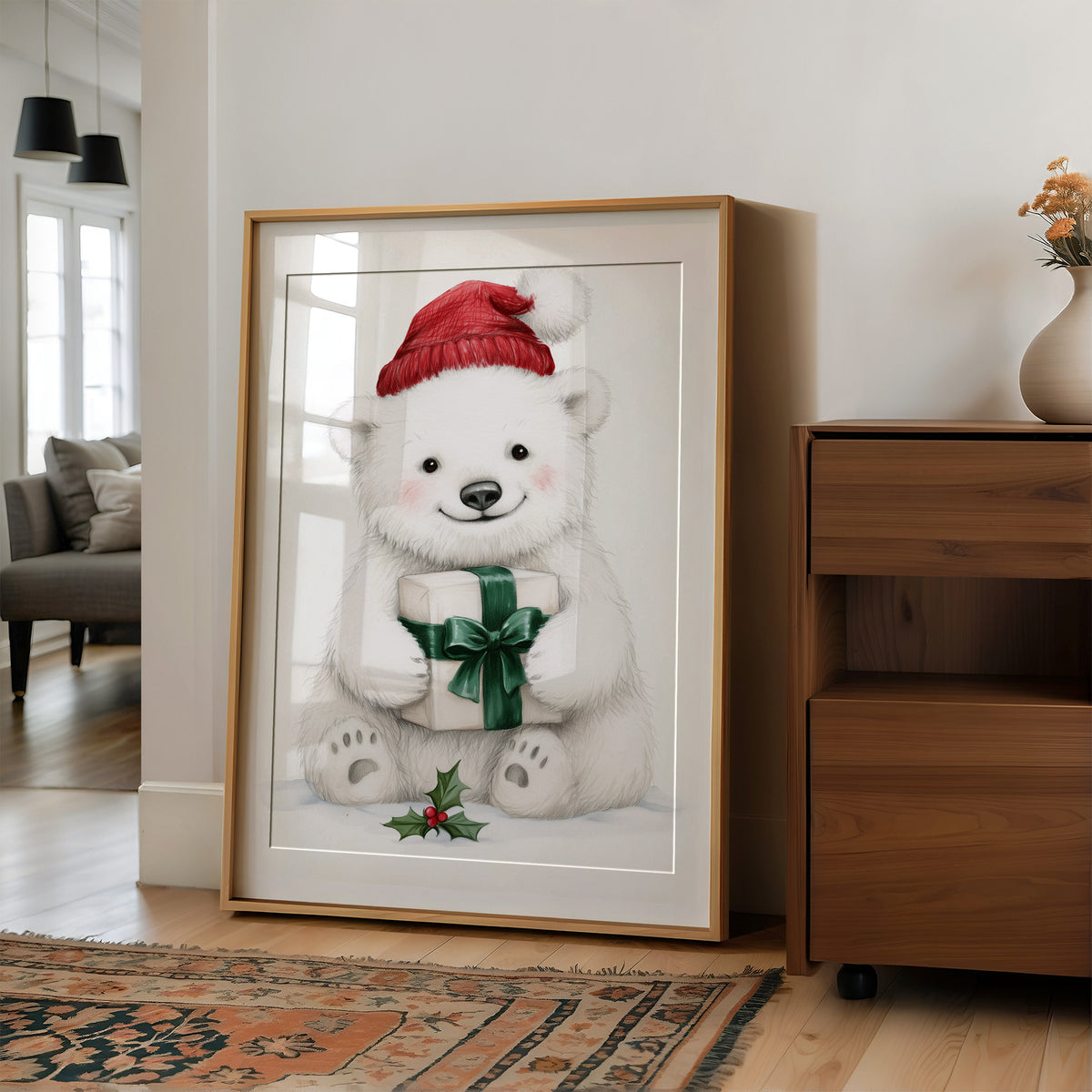 The Bear Cub Keeps a Secret, a small polar bear cub in a red knit hat hugging a green wrapped gift with a sprig of holly at its feet, on a soft cream ground, in a wood frame on a wall beside a walnut cabinet and an open doorway