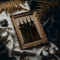The Coven Keeps Its Silence, five witches in tall pointed hats standing shoulder to shoulder, painted in black, charcoal and dusty cream, in an antique gold frame laid on white linen with ferns and a pocket watch