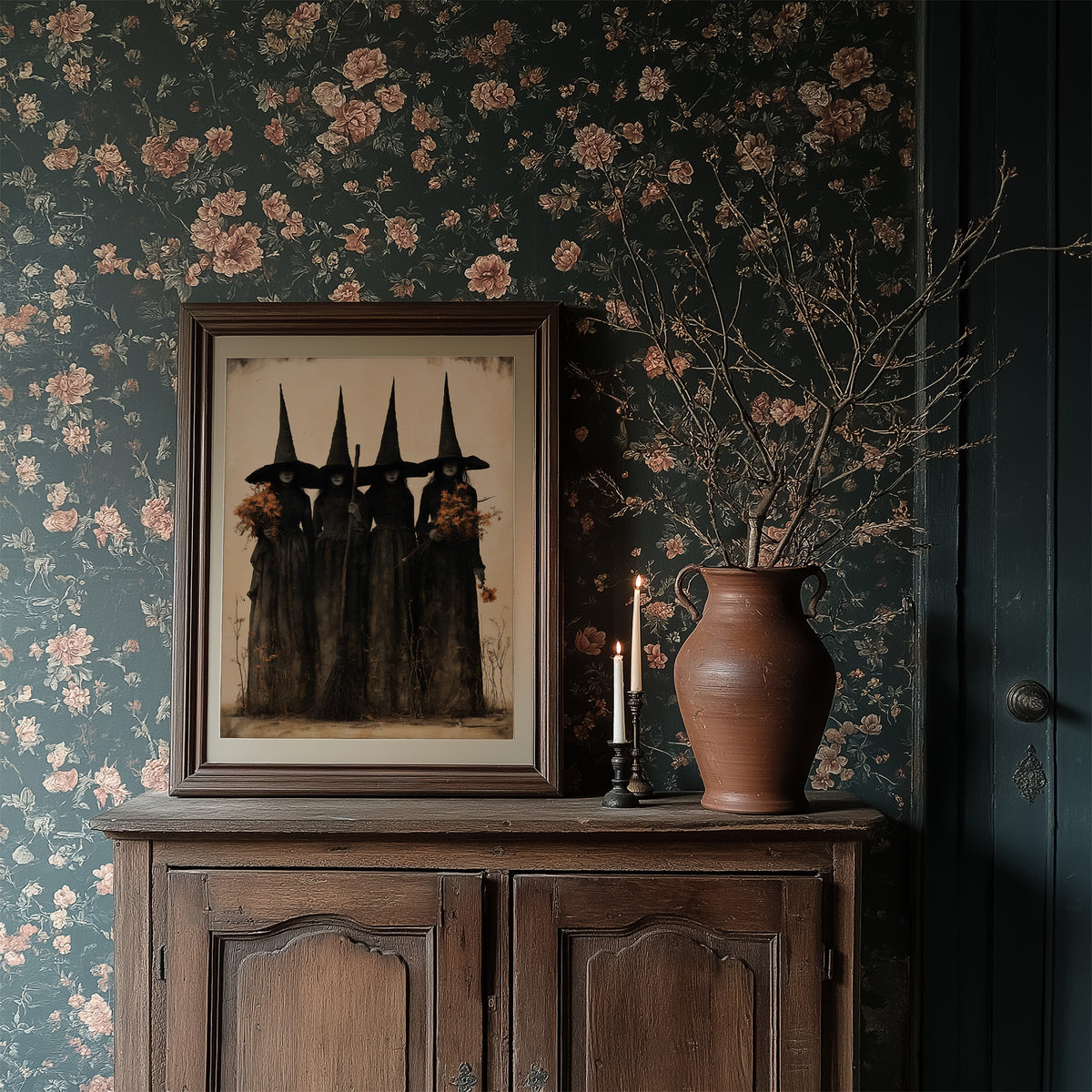The Coven Keeps Its Silence, five witches in tall pointed hats standing shoulder to shoulder, painted in black, charcoal and dusty cream, in a dark frame on a cabinet against floral wallpaper