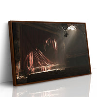 The Hall Waits for Its Audience, a dark interior lit by a single spotlight, rosy glowing forms rising out of deep shadow, as a framed canvas in a brown frame