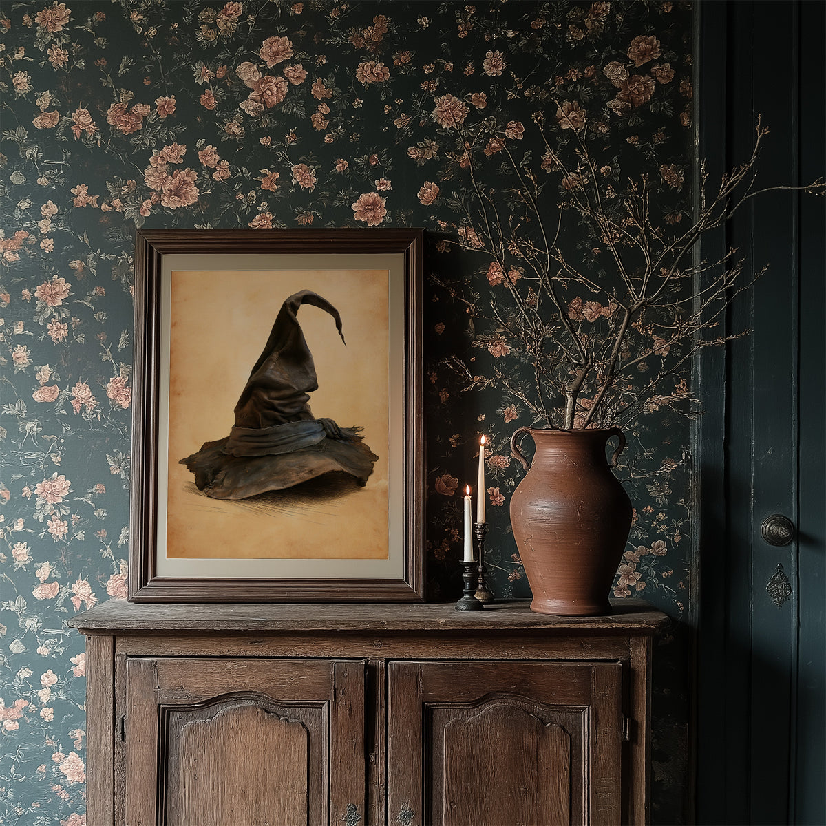 The Hat Left by the Door, a single pointed witch hat with a soft bend at the tip, sitting on a worn cream ground, painted in charcoal, brown and tan, in a dark frame on a cabinet against floral wallpaper
