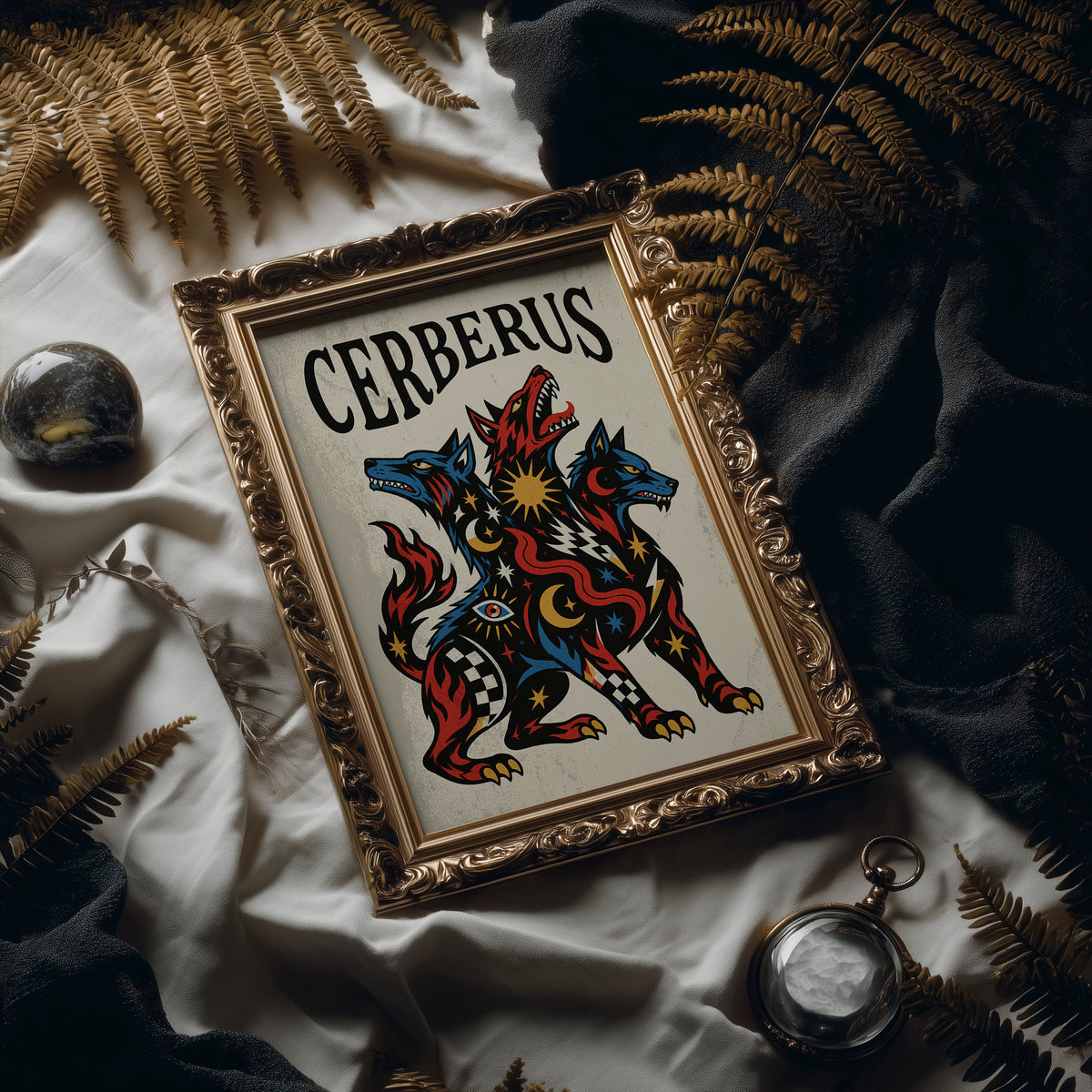 The Hound at the Threshold, a hound with several heads in red, blue and gold, with dark outlines and star and moon marks, in a bold flash sheet style with a black lettered name across the top, in an ornate frame on silk cloth beside ferns and a brass compass