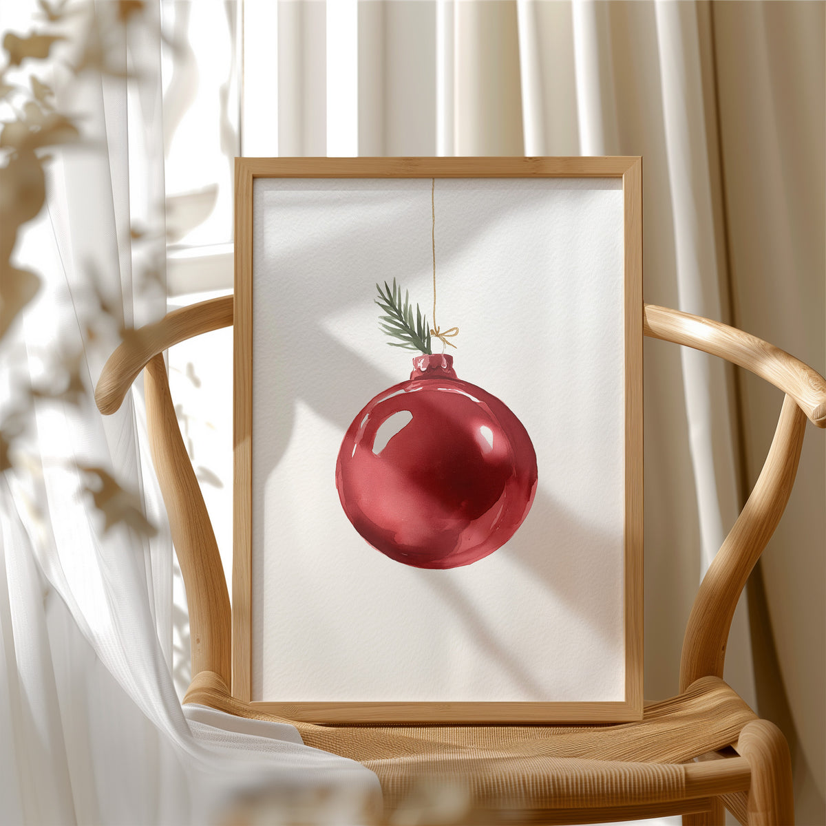 The Last Bauble on the Branch, a single red glass ornament hanging from a thin cord with a sprig of pine tip, on a cream ground, in a wood frame beside a wicker chair by a sunny window