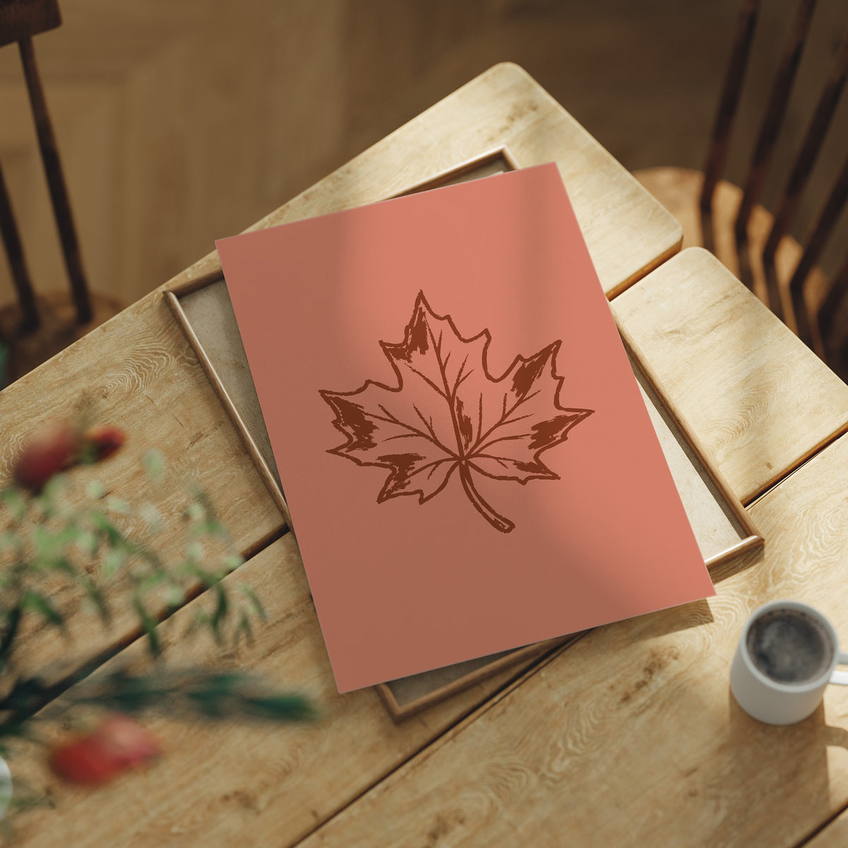 The Maple Keeps Its Last Light, a single maple leaf drawn in fine brown outline on a dusty terracotta ground, a botanical line study with soft shading, lying flat on a light wood table beside a coffee cup and red berries