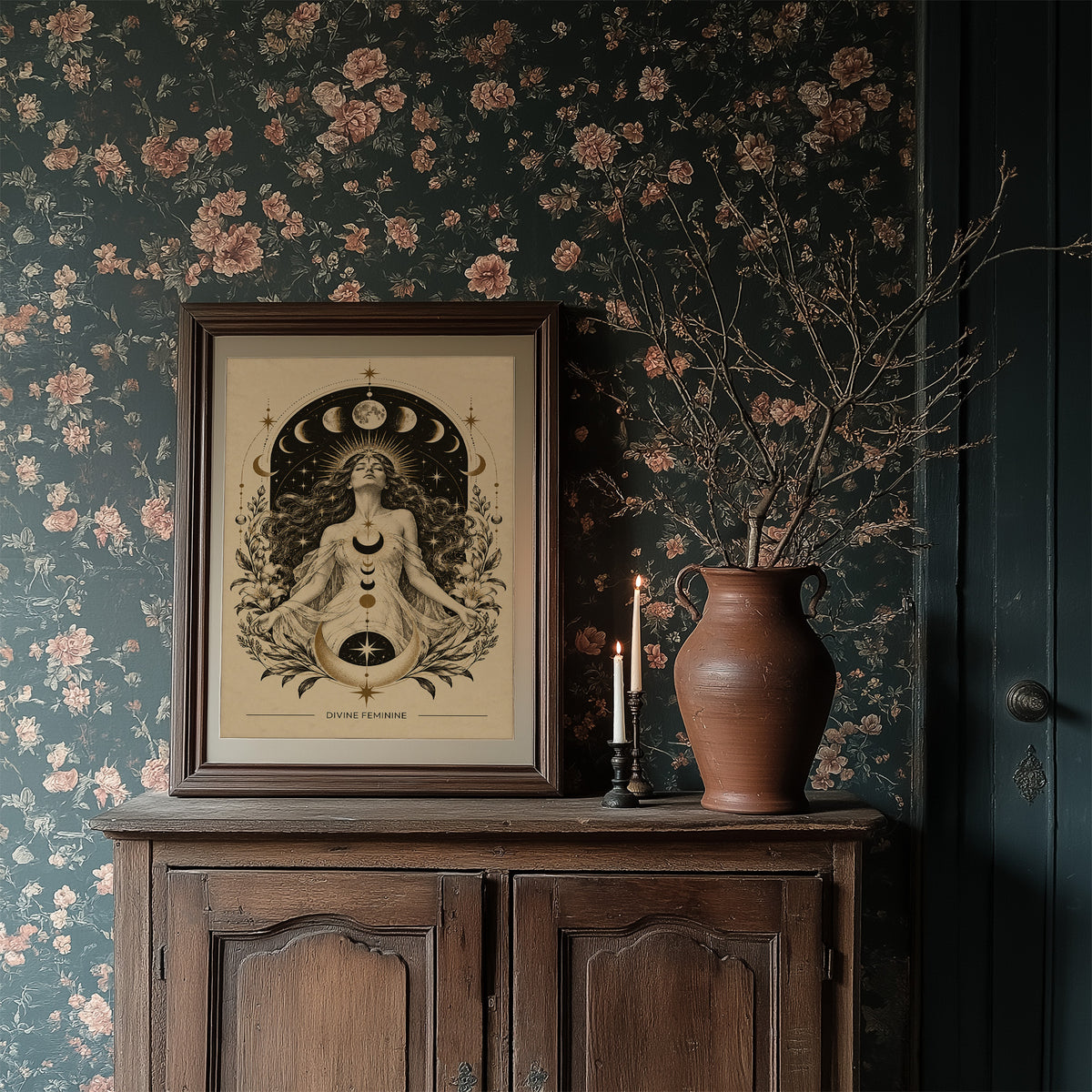 The Moon Woven Into Her Hair, a seated woman in quiet meditation crowned with a ring of crescent moons and surrounded by fern fronds, drawn in cream, charcoal and sepia with a deep brown border and small text at the base, in a dark wood frame on a floral wallpaper wall above a rustic cabinet and a vase