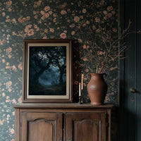 The Old Oak Keeps Its Midnight, gnarled trees rising out of a blue mist on a moonlit night, painted in deep navy, pale fog and charcoal shadow, in a dark frame on a wooden dresser against floral wallpaper
