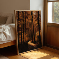 The Path Bends Toward Home, an autumn forest path winding between tall dark trunks, lit by a shaft of golden light across the leaves, painted in rust, amber and deep brown, leaning on a wood floor in a bedroom beside white linen bedding