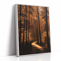 The Path Bends Toward Home, an autumn forest path winding between tall dark trunks, lit by a shaft of golden light across the leaves, painted in rust, amber and deep brown, as a framed canvas in a white frame