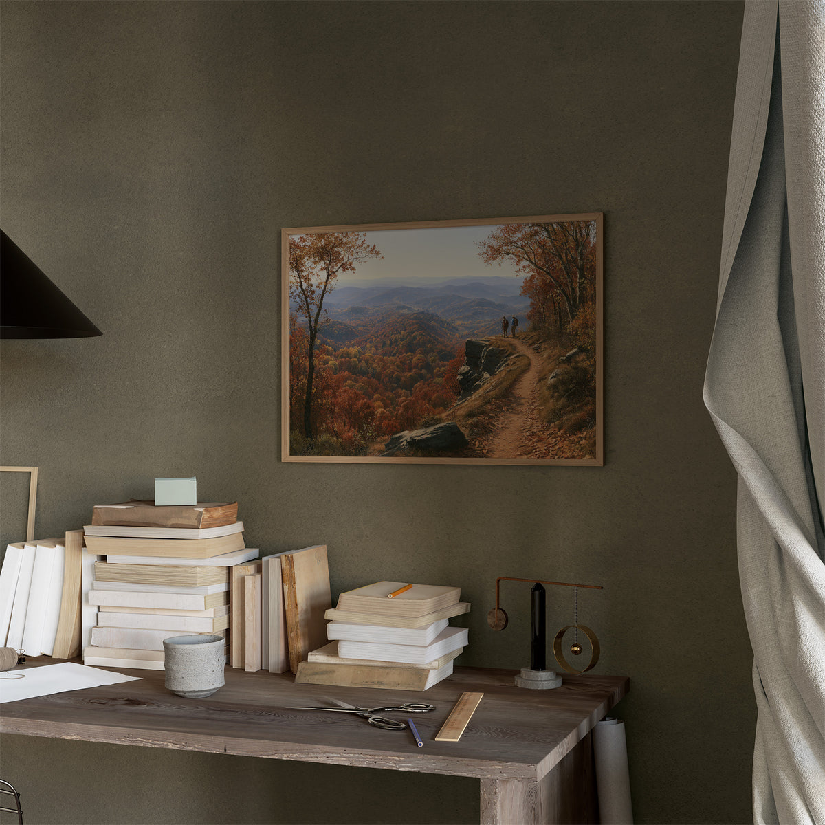 The Path Climbs Into October, a winding trail through copper autumn trees rising toward far blue hills, landscape oil painting, in a thin wood frame on a moss green wall above a desk stacked with books