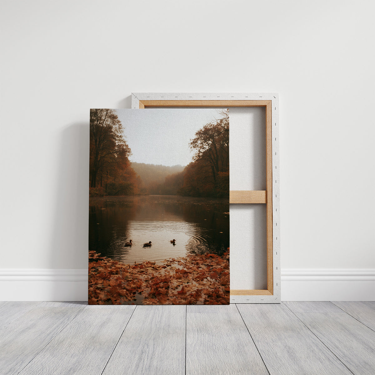The Pond Keeps Its Quiet Company, two ducks on a still misty lake among rust trees, a bank of fallen autumn leaves in the foreground, painted in rust, forest green and soft gold, on a gallery canvas with wrapped edges leaning against a white wall
