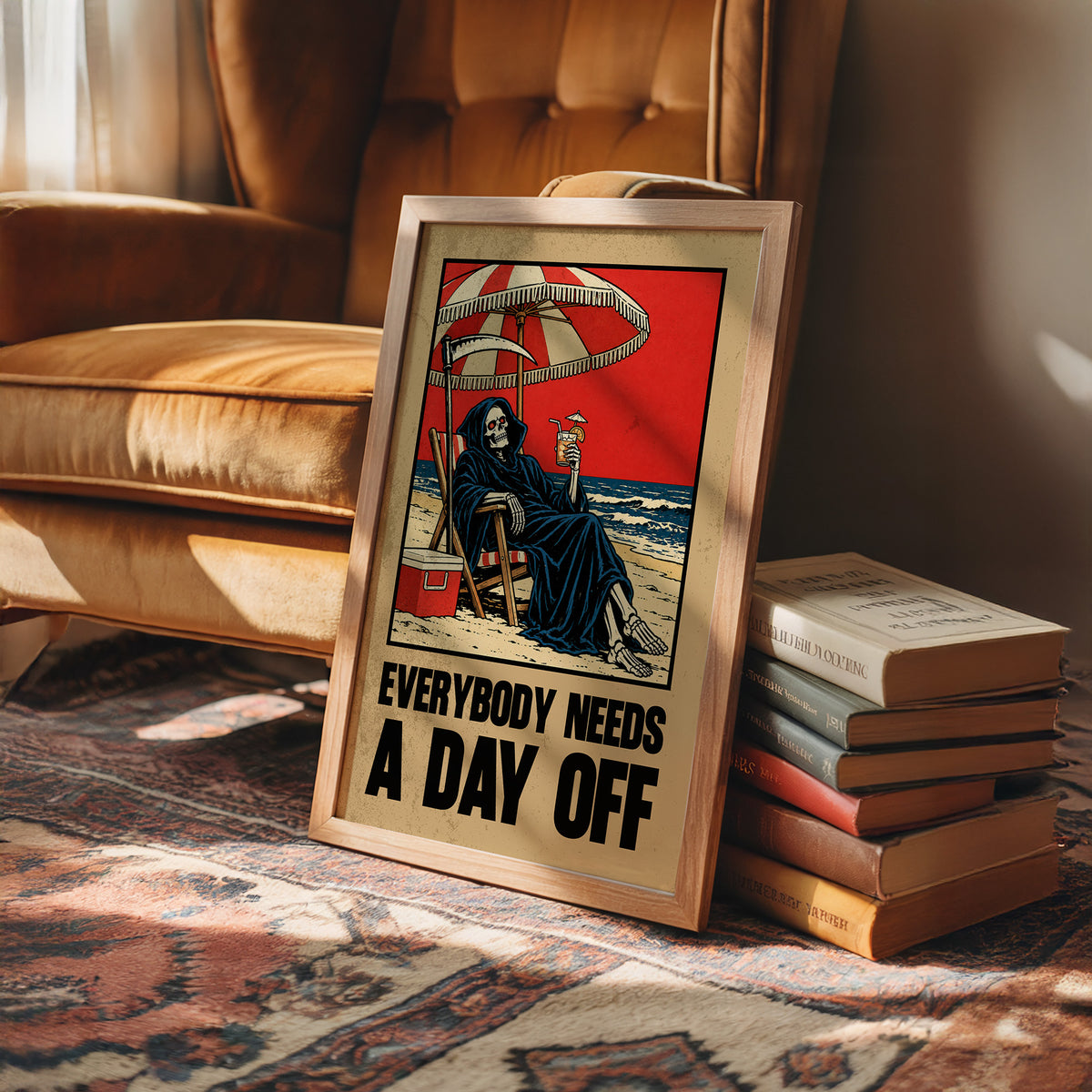 The Reaper Takes a Day Off, a hooded grim reaper in a deck chair under a striped umbrella on a red and cream beach poster, with the lettering EVERYBODY NEEDS A DAY OFF in bold black and tan below, in a retro print style, in a wood frame on a rug beside a leather armchair and stacked books