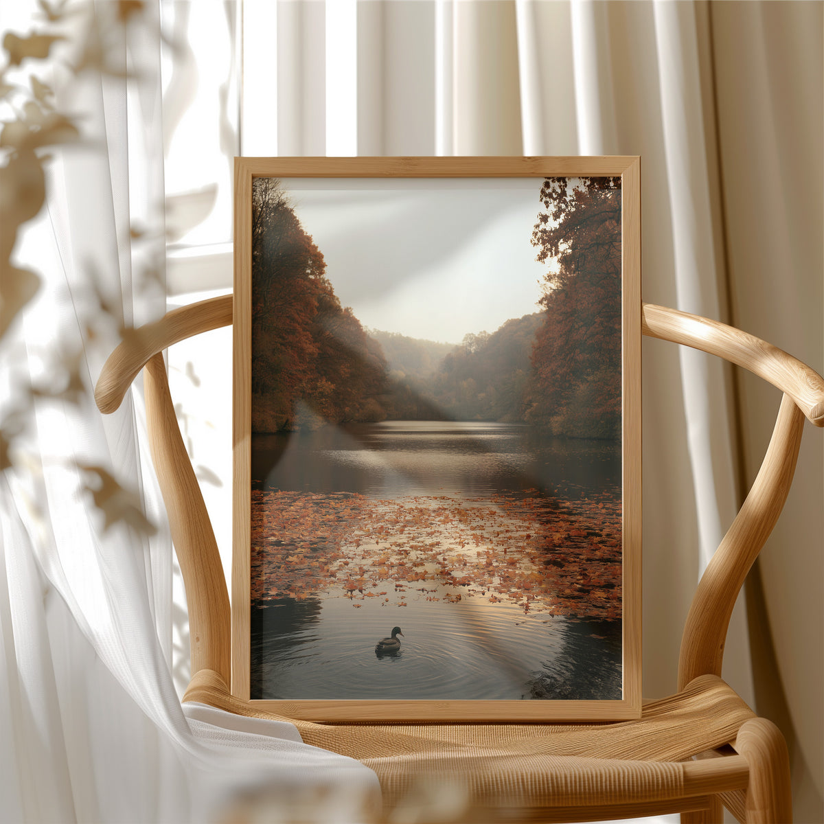 The Swan Waits on the Lake, a lone swan drifting on still water under turning autumn trees, with fallen leaves on the shore and a hazy golden light, painted in rust, amber and soft slate, in a wood frame beside a wicker chair by a sunny window