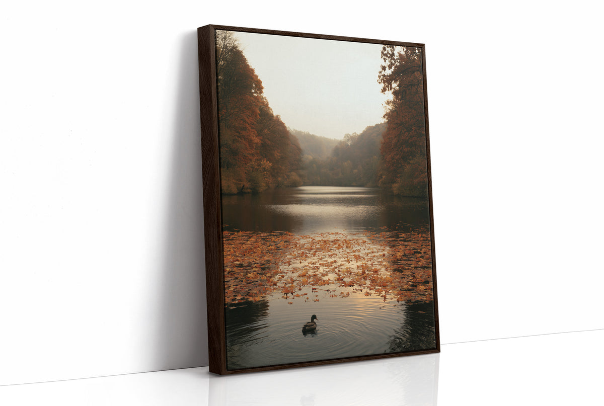 The Swan Waits on the Lake, a lone swan drifting on still water under turning autumn trees, with fallen leaves on the shore and a hazy golden light, painted in rust, amber and soft slate, as a framed canvas in a brown frame