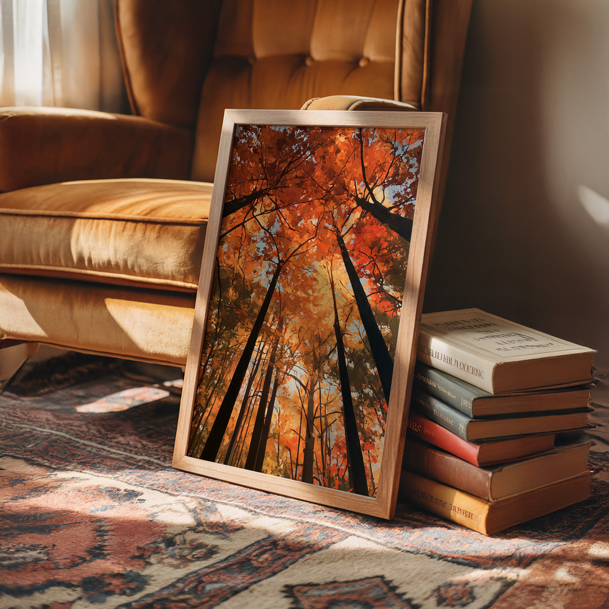 The Woods Blaze Overhead, a looking up view of tall trees with fiery red and orange autumn canopy and a sky of soft light, painted in flame red and burnt gold, in a wood frame on a rug beside a leather armchair and a stack of books