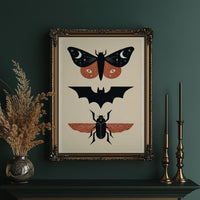 Three Night Visitors in a Row, a moth with crescent moon spots, a black bat in flight and a beetle with rust wings stacked in a column on a cream ground, painted in black, rust and cream, in an ornate gold frame on a deep green wall beside tall brass candlesticks