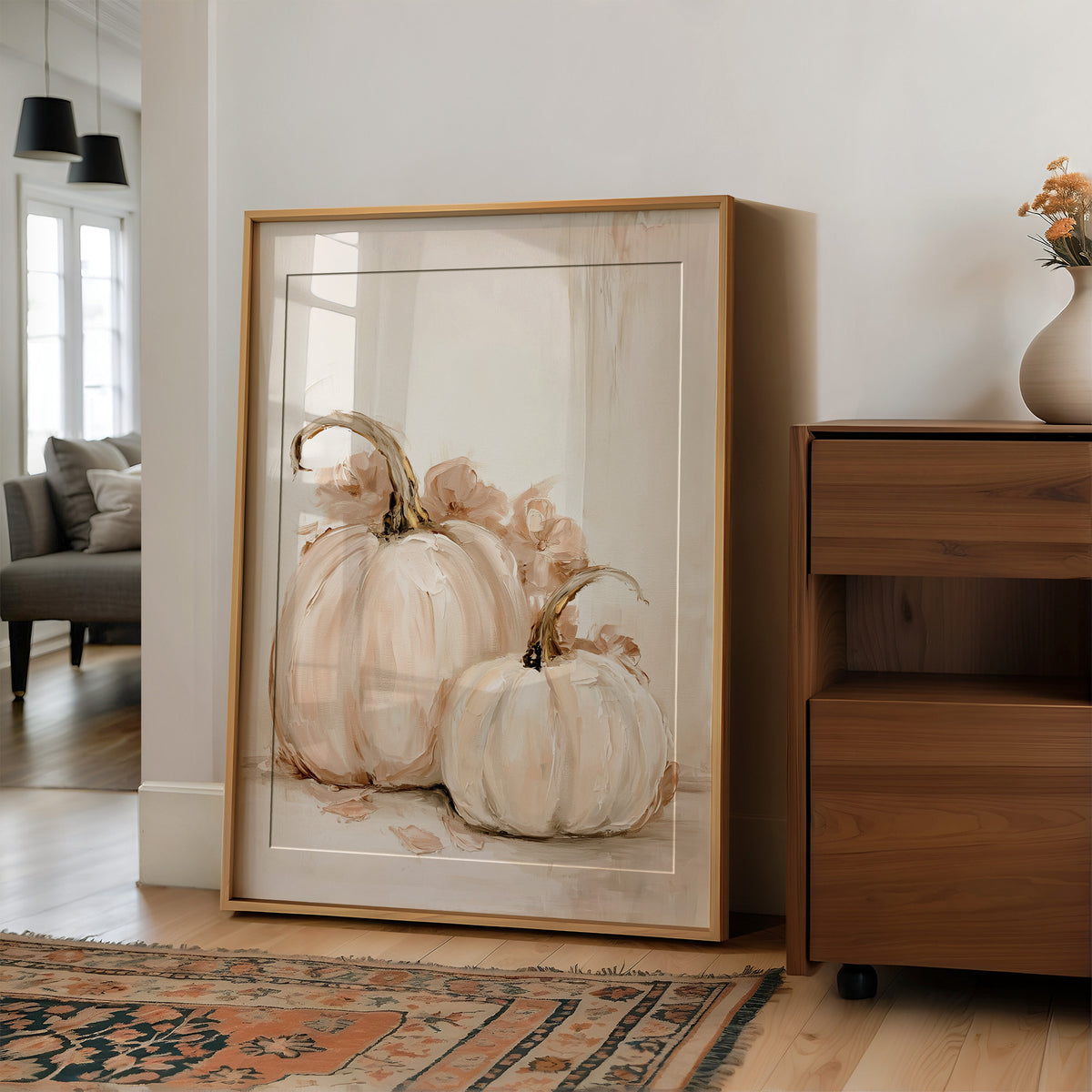 Two Pale Gourds Keep Company, two white pumpkins with curling stems and soft peach shadows on a cream ground, painted in ivory, blush and sage, in a wood frame on a wall beside a walnut cabinet and an open doorway