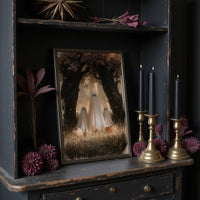 Two Visitors Under the Arch, two pale ghosts standing under an arch of dark trees above a field of tall grass and fallen leaves, painted in deep brown, bone and moss, in a dark frame on a black shelf beside brass candles and dried leaves