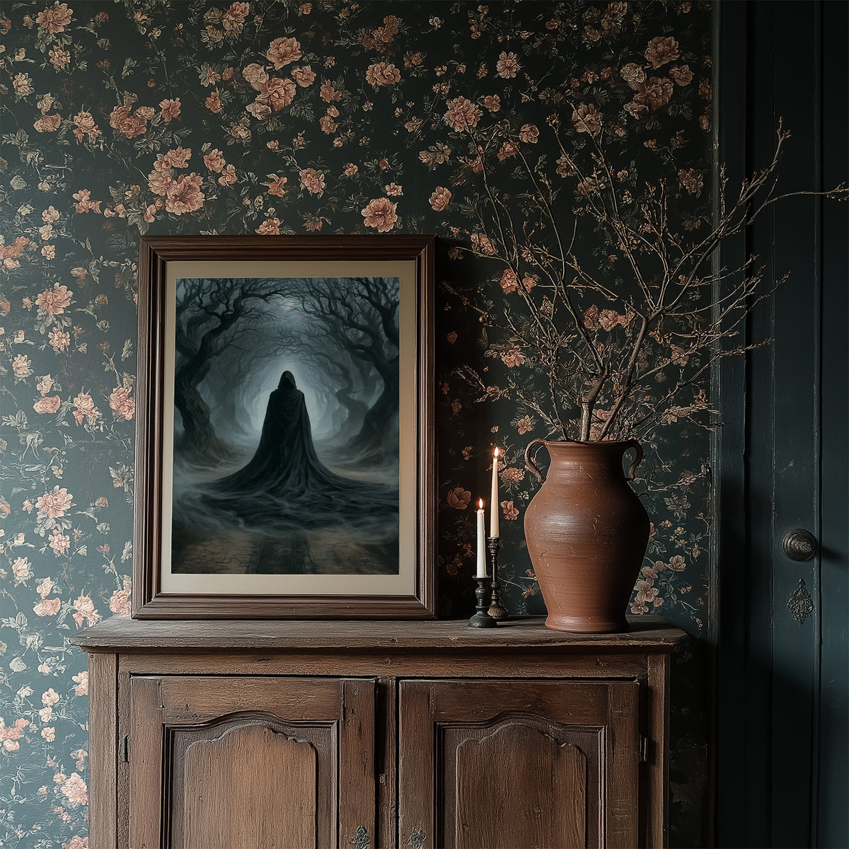 Veiled Beneath the Bending Trees, a hooded robed figure standing at the end of a tunnel of bare trees in pale blue fog, in a dark frame on a wooden dresser against floral wallpaper