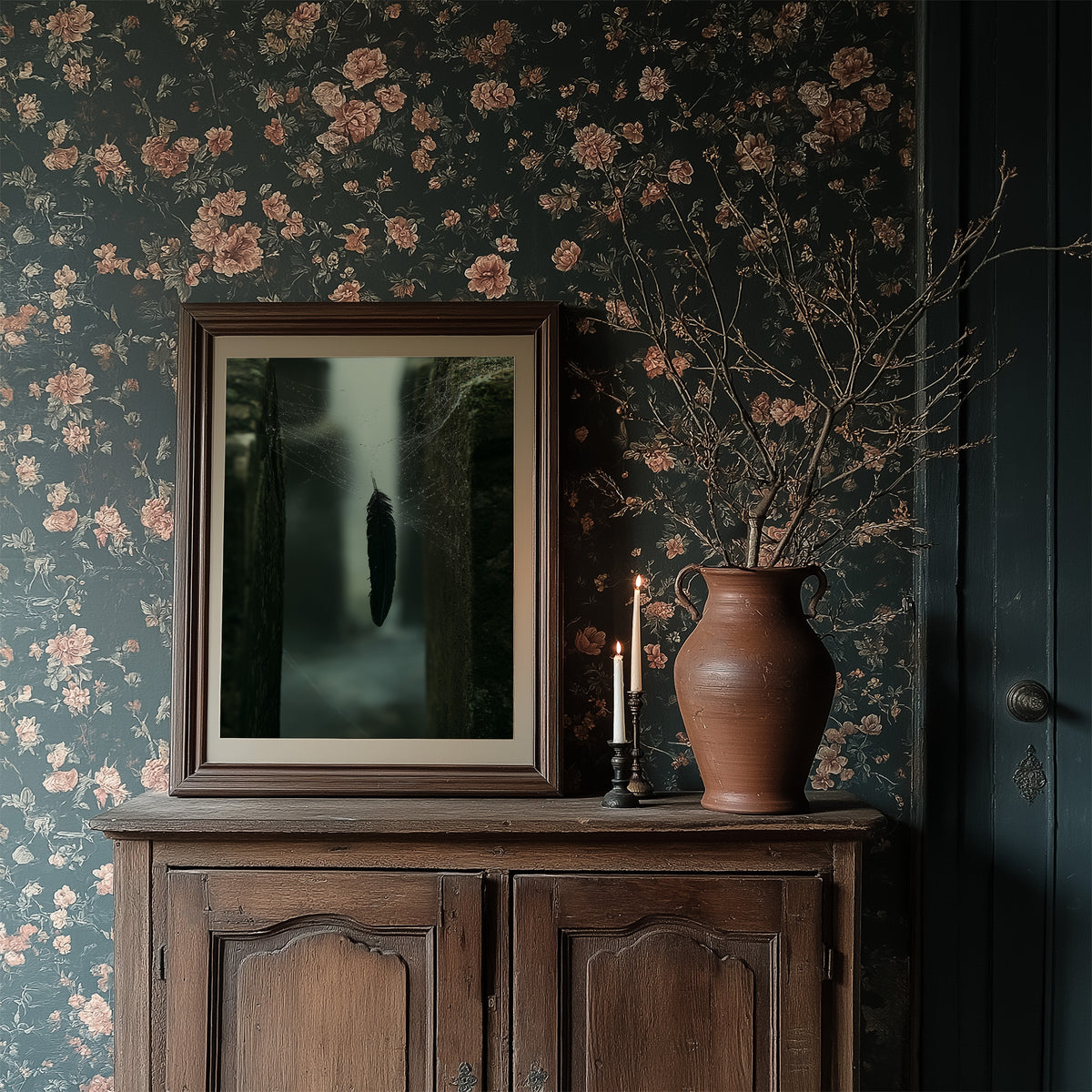 Where the Mist Leaves a Door Open, a narrow path between tall dark trees in pale fog, a single dark cypress at the center, deep green and charcoal moody landscape, in a dark frame on a wooden dresser against floral wallpaper
