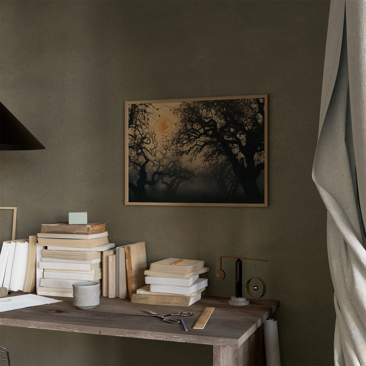 Where the Old Oak Keeps Watch, a bare twisted tree silhouetted against an amber full moon above a misty dark forest, in a thin wood frame on a moss green wall above a desk stacked with books