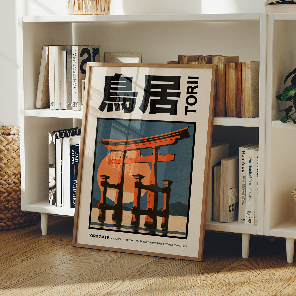 Where the Tide Meets the Posts, a vermilion torii shrine gate standing in shallow teal water beneath a bright orange sun, in a flat Japanese travel poster style with bold black lettering, painted in vermilion, teal and cream, in a wood frame on a white bookshelf beside stacked books and a small basket