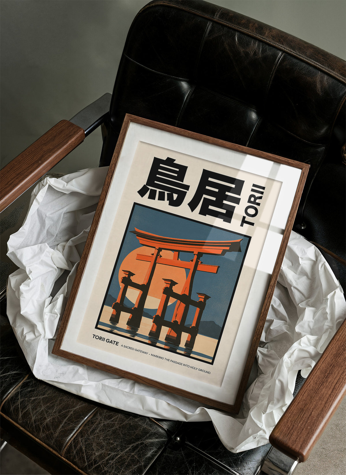 Where the Tide Meets the Posts, a vermilion torii shrine gate standing in shallow teal water beneath a bright orange sun, in a flat Japanese travel poster style with bold black lettering, painted in vermilion, teal and cream, in a wood frame on a black leather armchair beside crumpled white tissue
