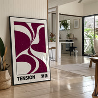Where Two Curves Almost Touch, two maroon curved forms on a cream ground that lean toward each other and almost meet, with the word TENSION in black capitals and a small Japanese word beside it, in a black frame leaning on a bright hallway floor beside a potted plant