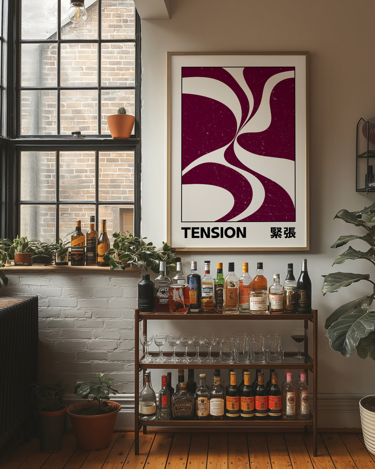 Where Two Curves Almost Touch, two maroon curved forms on a cream ground that lean toward each other and almost meet, with the word TENSION in black capitals and a small Japanese word beside it, in a wood frame on a brick wall above a bar cart of bottles and plants