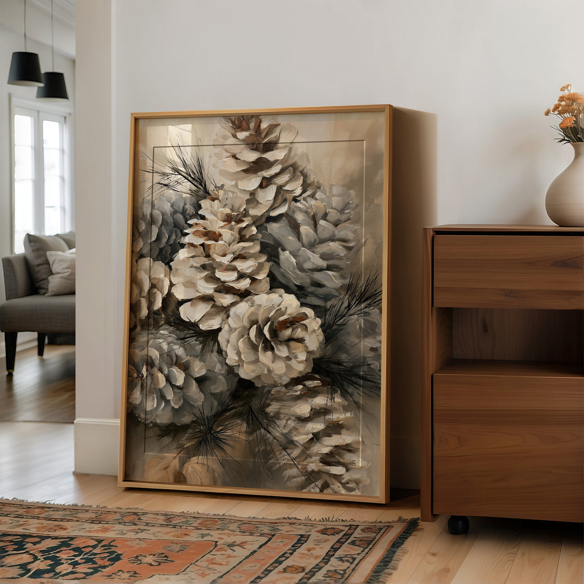 Winter Keeps Its Pine Cones, a cluster of pine cones on soft evergreen boughs, drawn in sepia, sage gray and warm bone with a natural history detail, in a wood frame on a wall beside a walnut cabinet and an open doorway