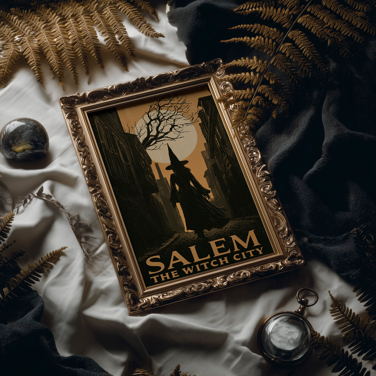 Witch City at Moonrise, a cloaked silhouette beneath a bare tree and a full moon on a vintage style travel poster, painted in amber, olive and black, in an antique gold frame laid on white linen with ferns and a pocket watch