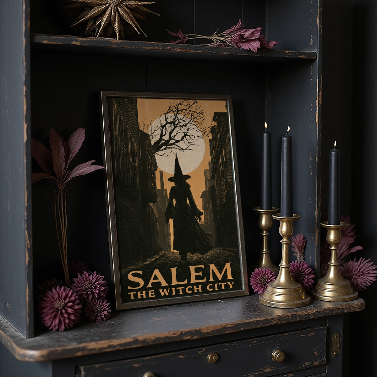 Witch City at Moonrise, a cloaked silhouette beneath a bare tree and a full moon on a vintage style travel poster, painted in amber, olive and black, on a dark wooden cabinet shelf with candles and dried flowers