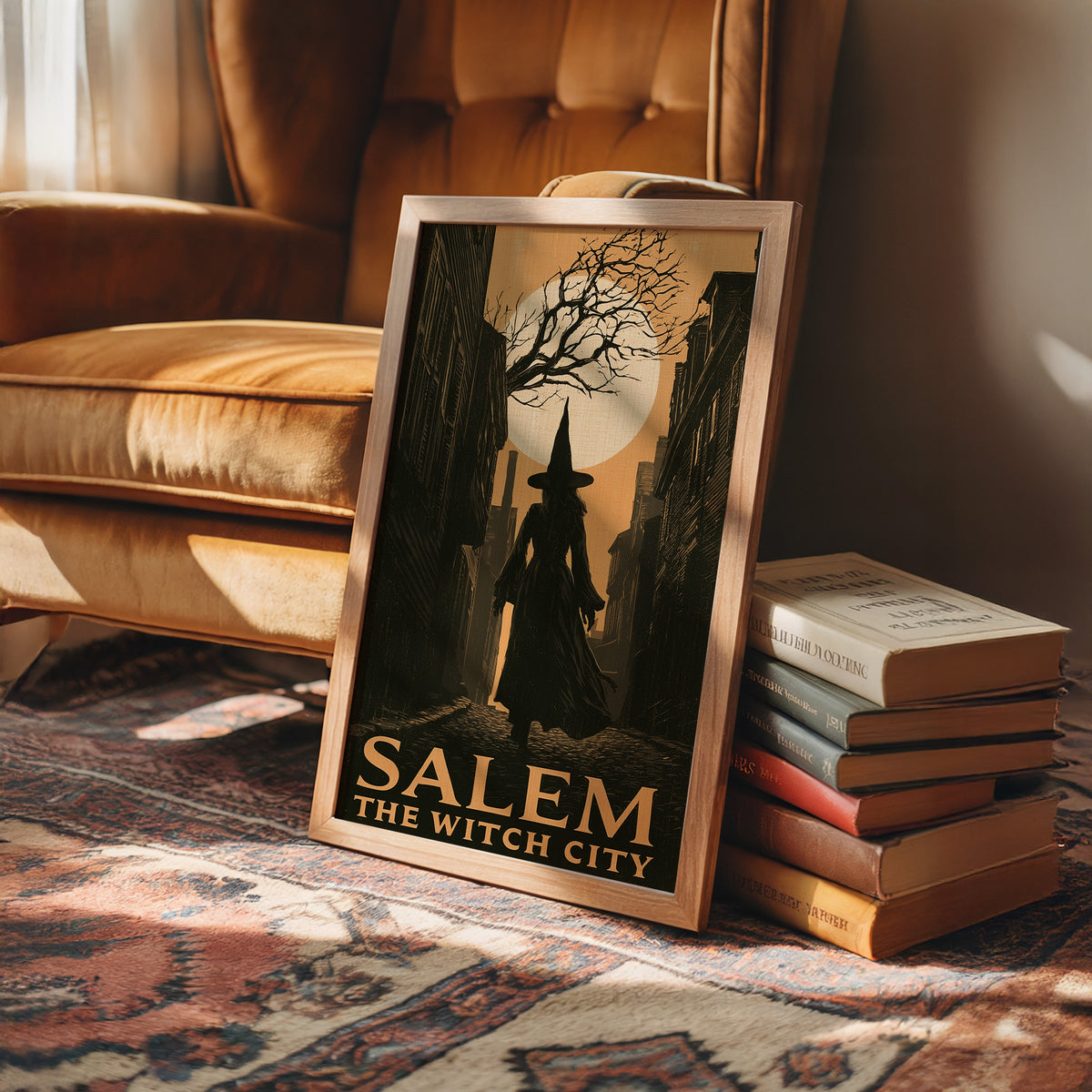 Witch City at Moonrise, a cloaked silhouette beneath a bare tree and a full moon on a vintage style travel poster, painted in amber, olive and black, in a wood frame beside a leather armchair and a stack of books